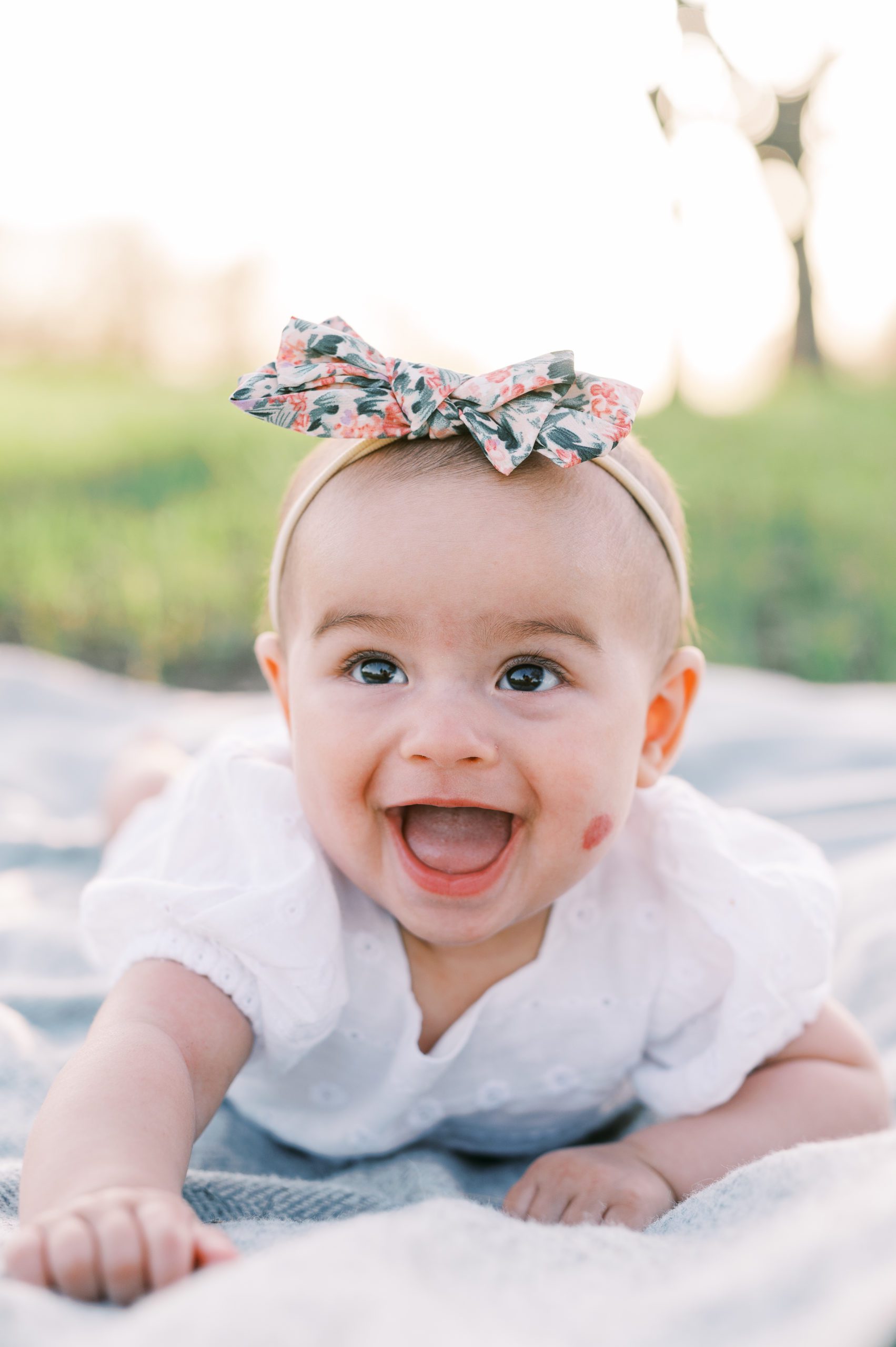 baby girl smiling with white outfit and floral headband in Minneapolis field