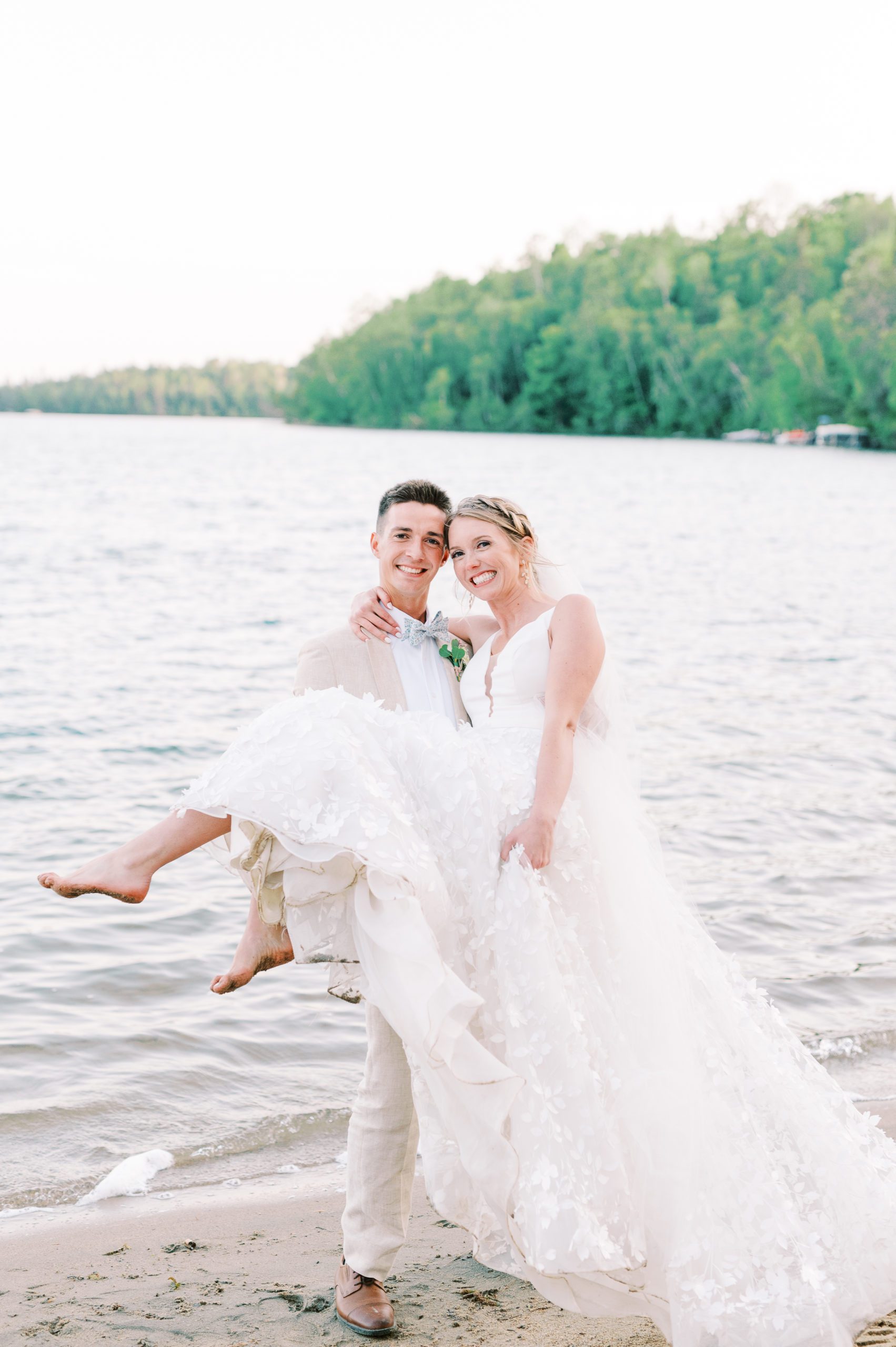 groom holds bride on beach