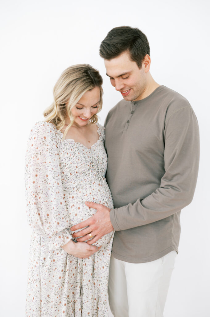 Mom and dad standing together holding mom's stomach at maternity session