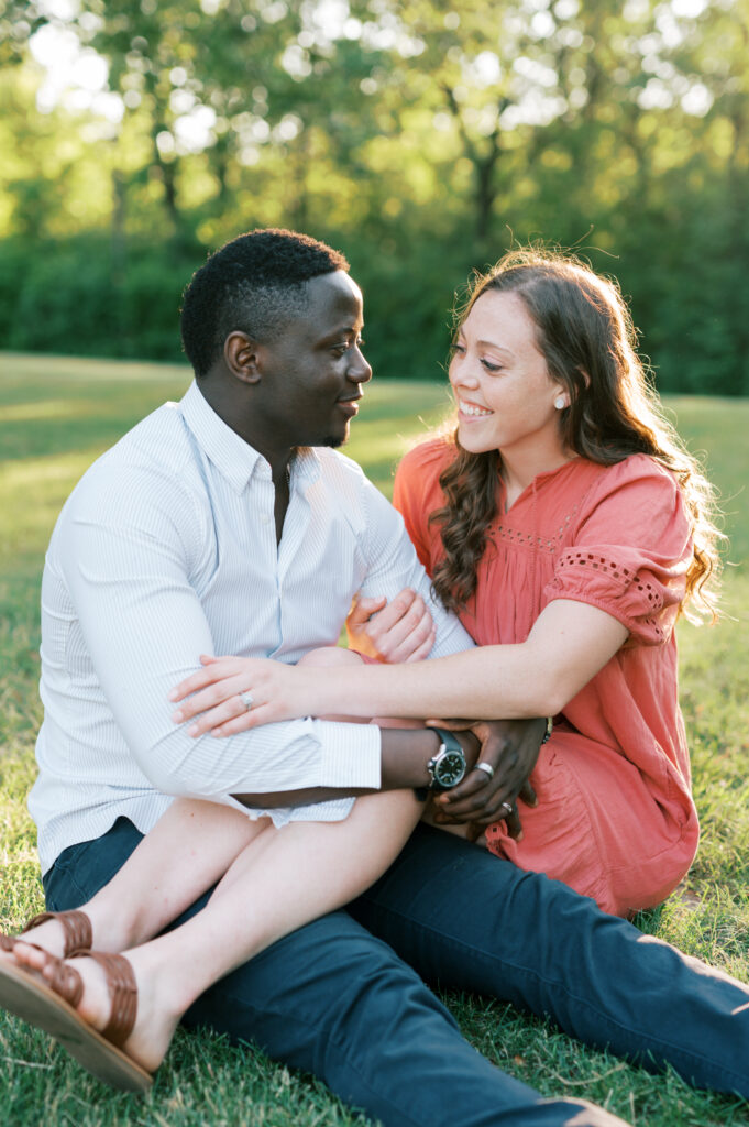 engagement session couple sitting in grass together looking at each other lovingly